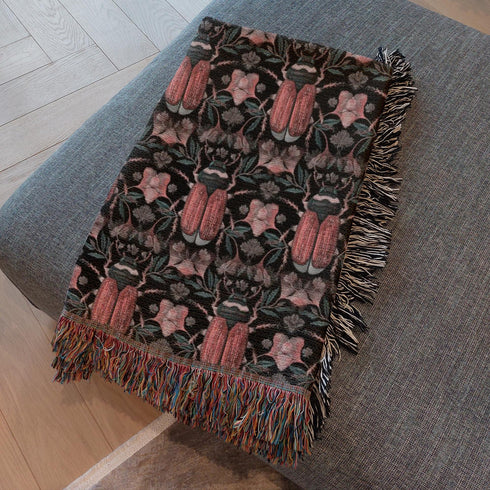 Luxurious woven cotton throw blanket featuring symmetrical scarab beetle pattern in terracotta on black background with white fringe detail. Perfect as gothic wall tapestry, dark academia decor, or cottagecore blanket for bedroom or living room.